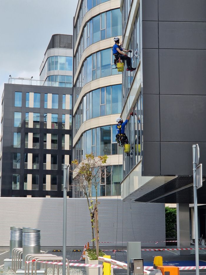 home-img Two workers clean windows on a tall office building in a city setting.