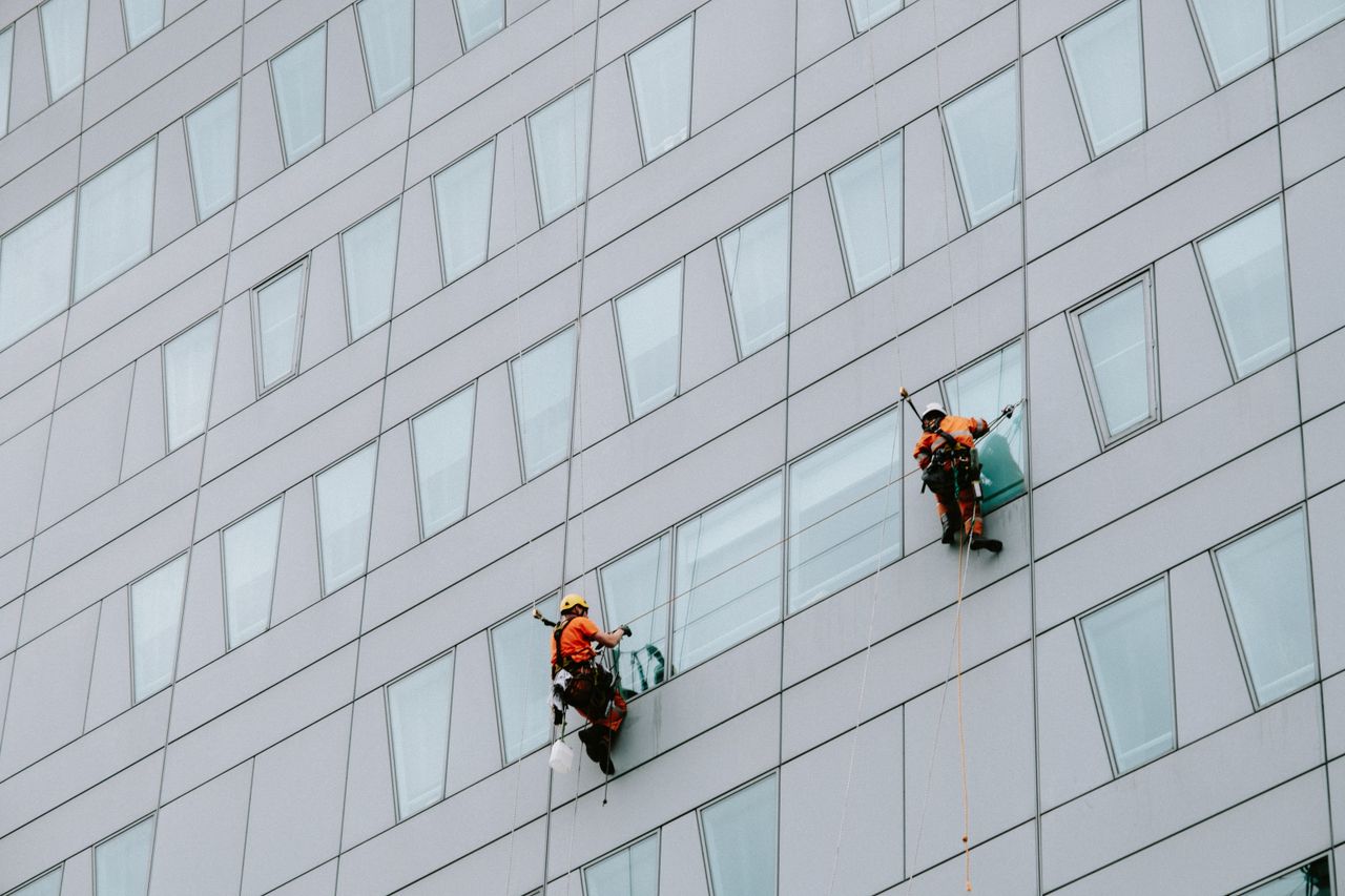 about-img-01 High-rise window washers in safety gear cleaning a skyscraper facade.